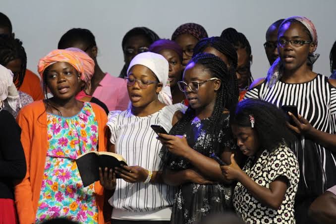 Young women singing together at a church gathering, one holding an open Bible